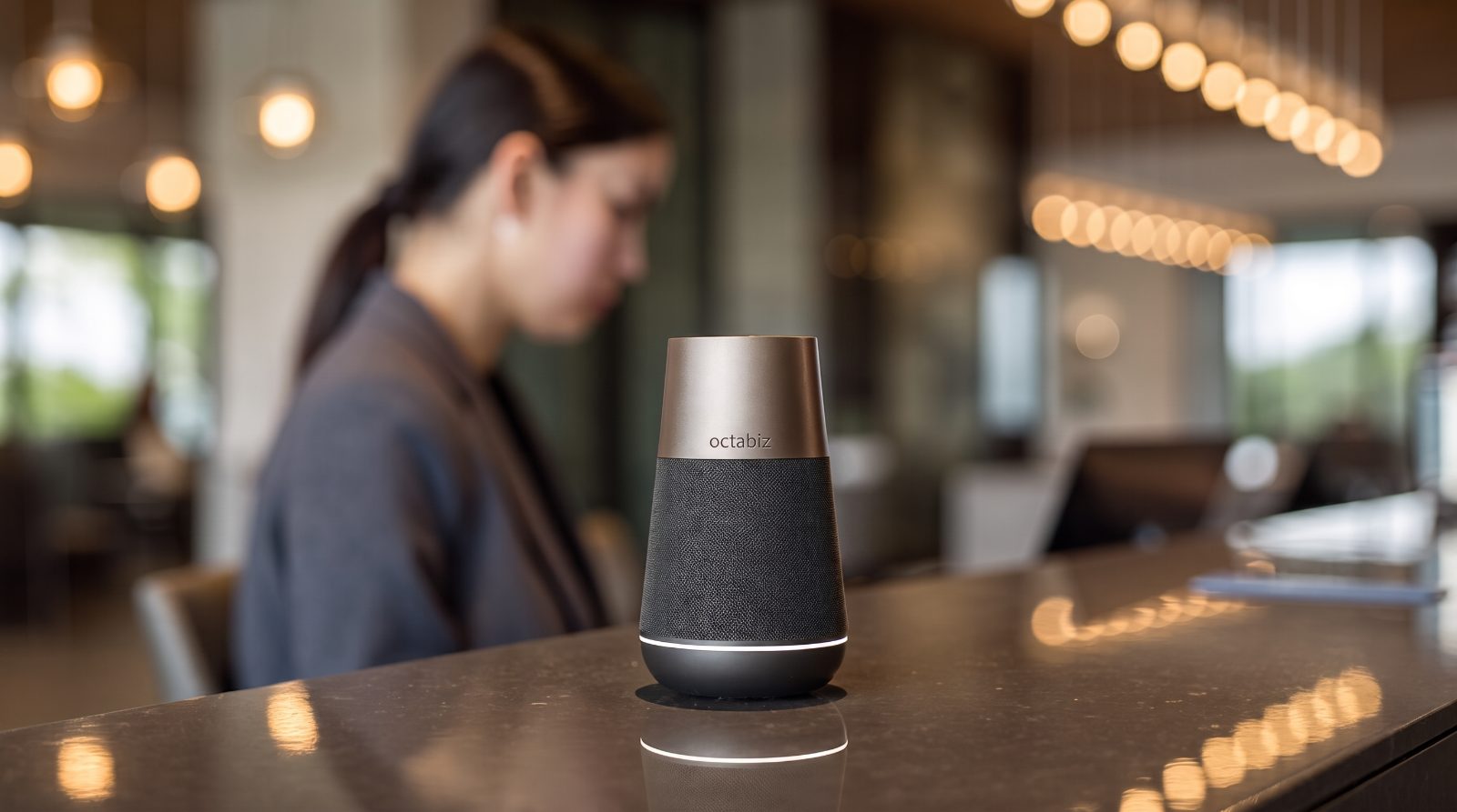 The Octabiz smart speaker sitting on a hotel reception desk, its light ring glowing as it listens, representing the shift from screens to conversational interfaces